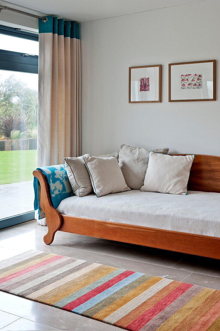 Holzliege mit gestreiftem Teppich am Fenster in einem modernen Haus, Cornwall, England, UK