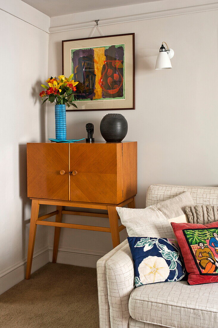 Vintage-Holzschrank und Kunstwerke mit Sofa im Wohnzimmer von Padstow cottage, Cornwall, England, UK