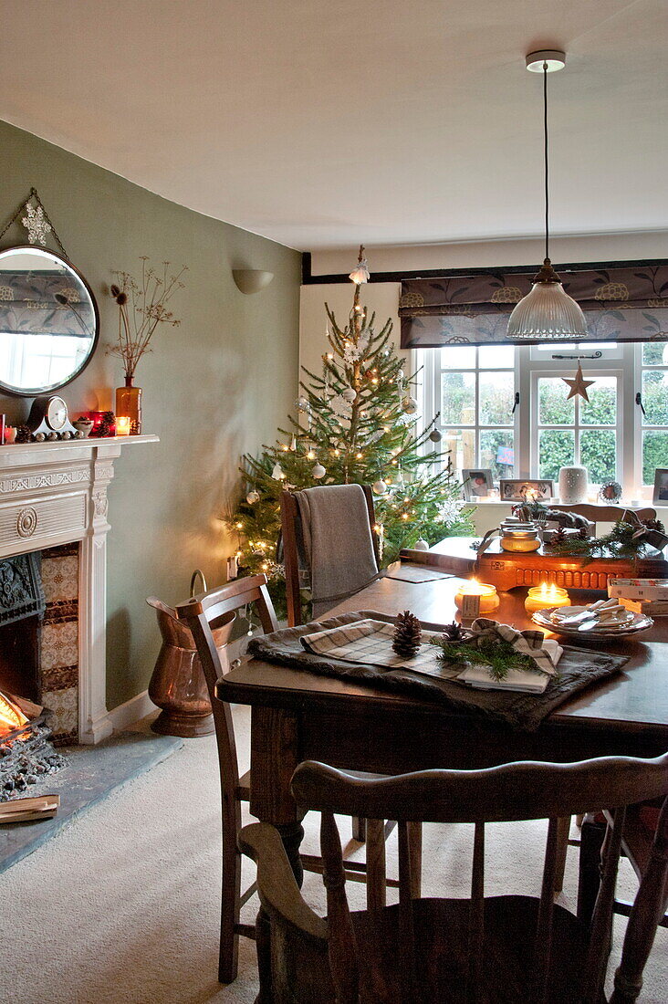 Beleuchtete Kerzen auf dem Esstisch mit Weihnachtsbaum in einem Landhaus in Shropshire, England, UK