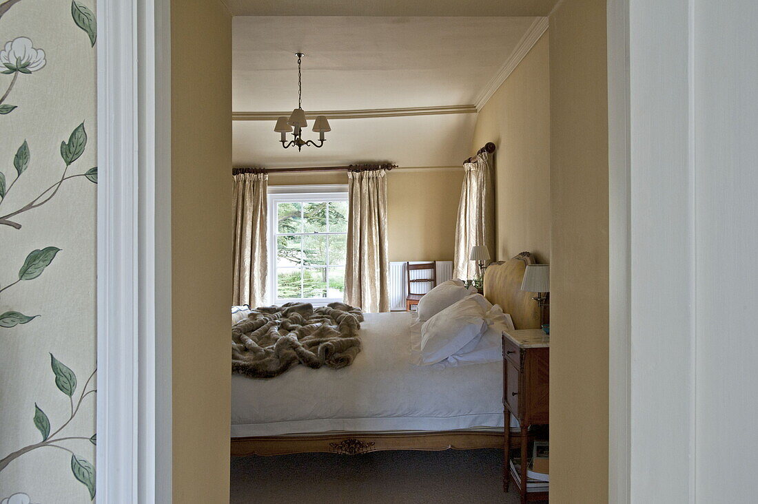 Blick durch die Tür zum Doppelbett mit Felldecke in einem modernen Landhaus in Suffolk, England, UK