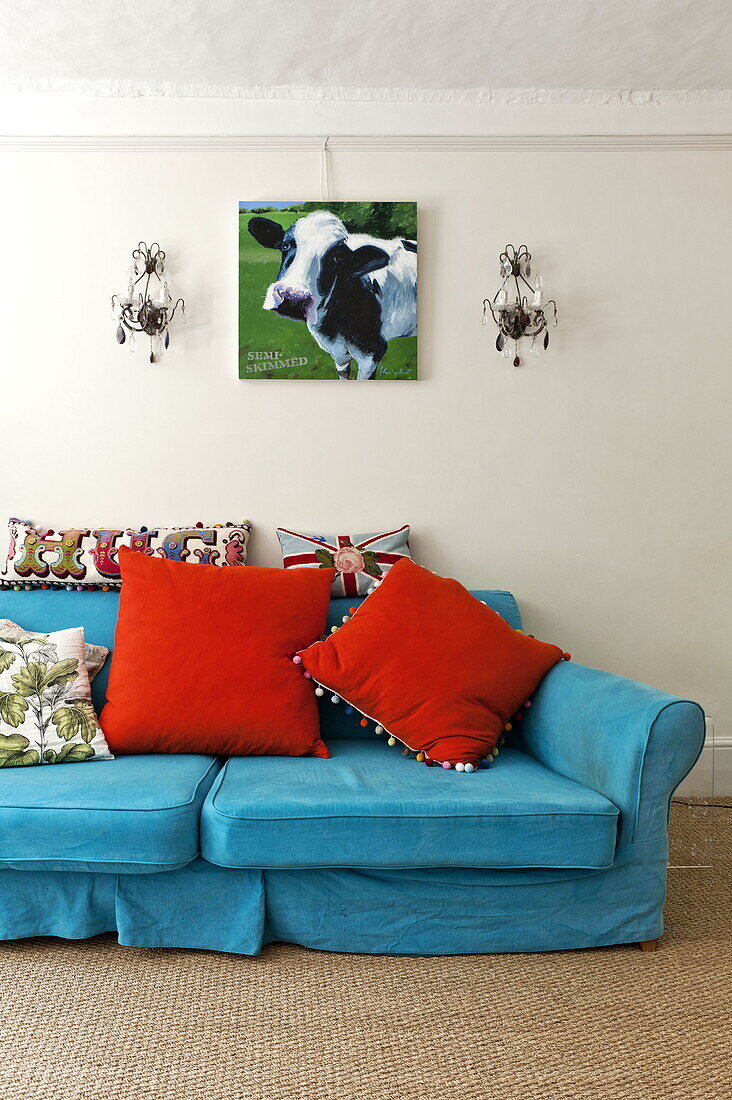 Knallbuntes Sofa und Kissen unter einem Kunstwerk mit einer Kuh in einem modernen Haus in Suffolk/Essex, England, UK