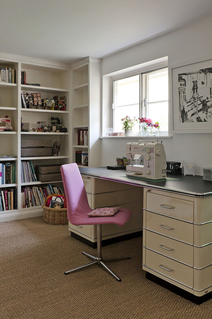 Pink chair at table with sewing machine in work room of contemporary Suffolk/Essex home, England, UK