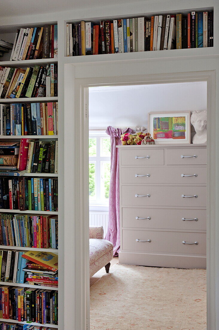Book storage with view through doorway to large chest of drawers in contemporary Suffolk/Essex home, England, UK
