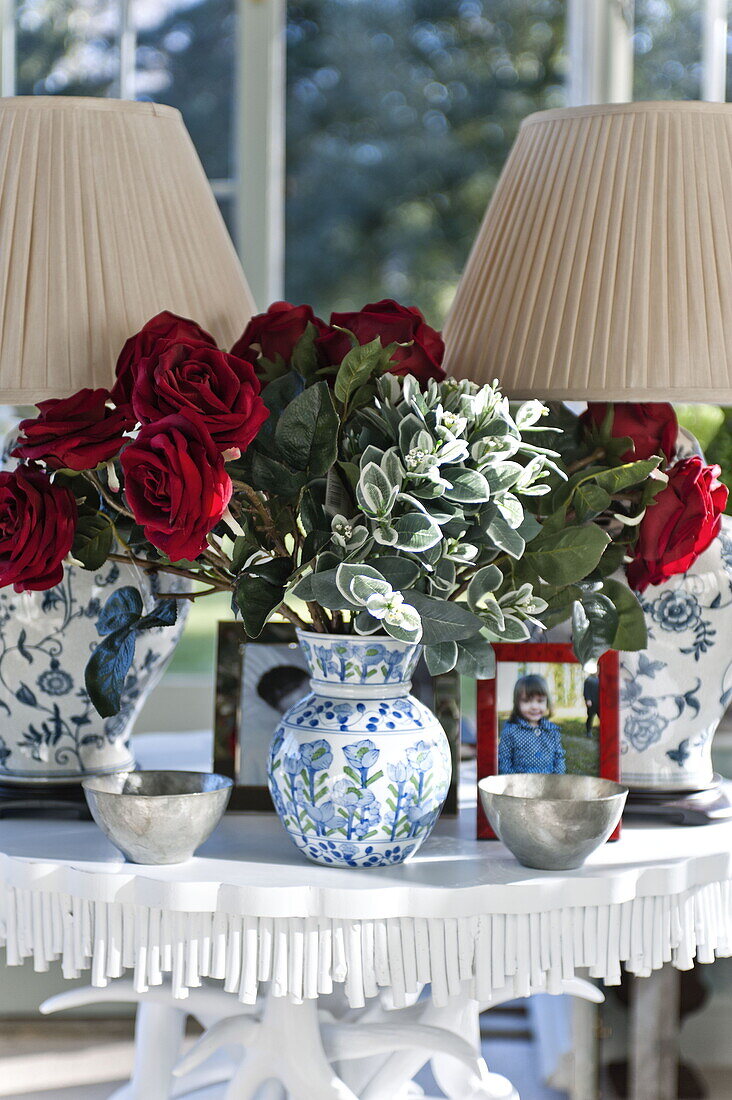 Rote Rosen mit blauen und weißen Keramiklampenvasen auf einem Tisch in einem Landhaus in Bury St Edmunds, Suffolk, England, UK