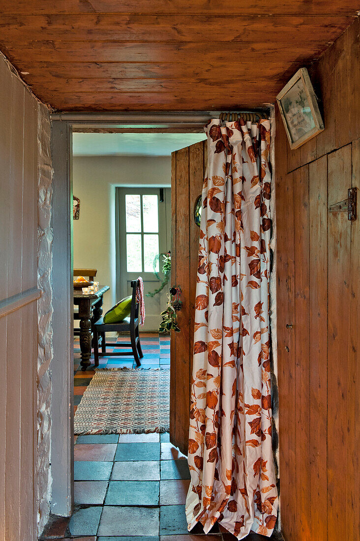 Blick durch eine mit Vorhängen versehene Tür vom holzgetäfelten Flur in die Küche eines Hauses in Tregaron, Wales, UK