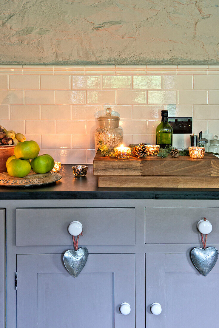 Beleuchtete Teelichter mit Äpfeln und Nüssen auf grauer Küchenarbeitsplatte mit silbernen Herzen in einem Haus in Tregaron, Wales, UK