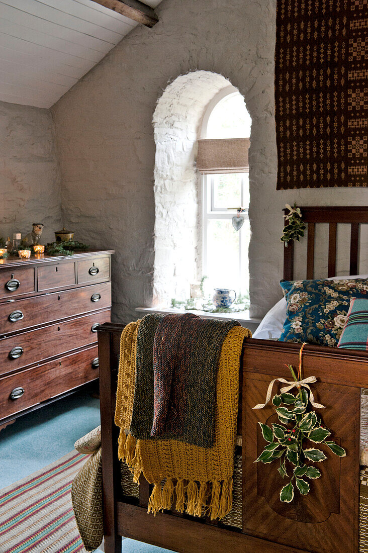 Gewölbtes Fenster mit Holzkommode und Decken auf dem Fußteil des Bettes in einem Haus in Tregaron, Wales, Vereinigtes Königreich