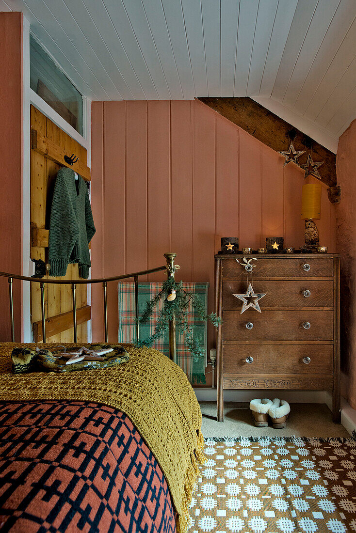 Holzkommode und gemusterte Bettbezüge in einem pfirsichfarbenen Schlafzimmer in einem Haus in Tregaron, Wales, UK