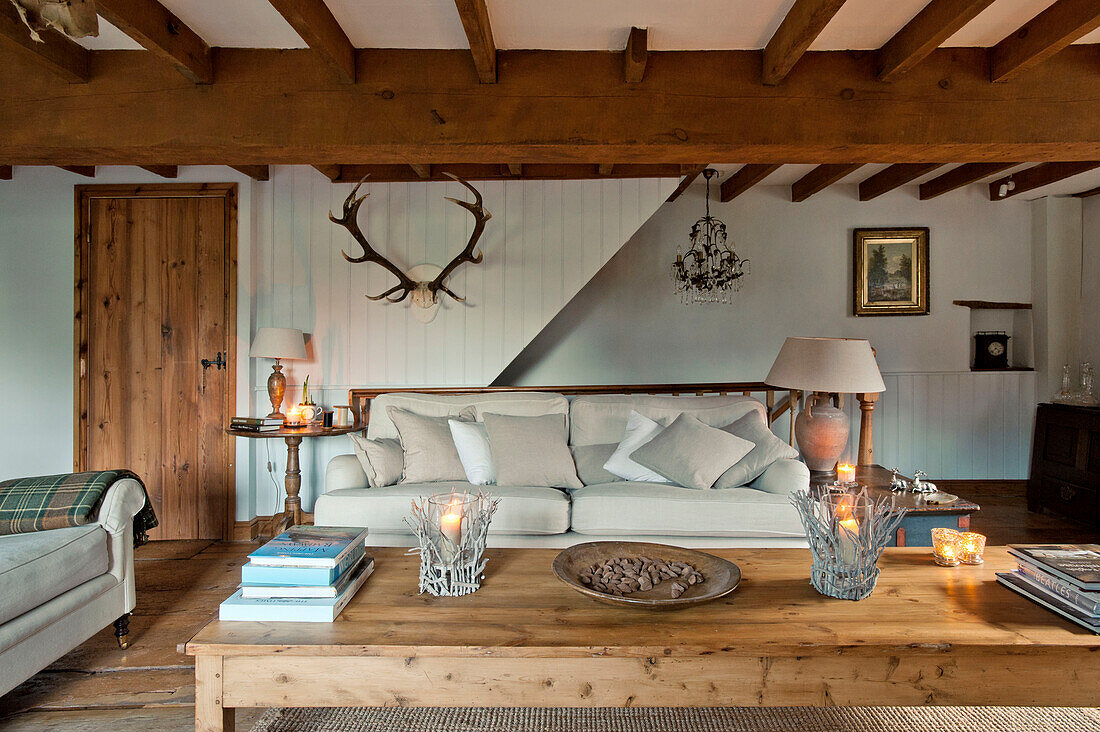 Books and lit candles on wooden coffee table in living room of Sherford barn conversion with wall-mounted antlers Devon UK
