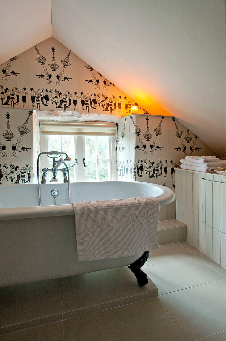 Freistehende Badewanne mit Mustertapete im Badezimmer im Dachgeschoss einer umgebauten Scheune in Sherford, Devon, Großbritannien