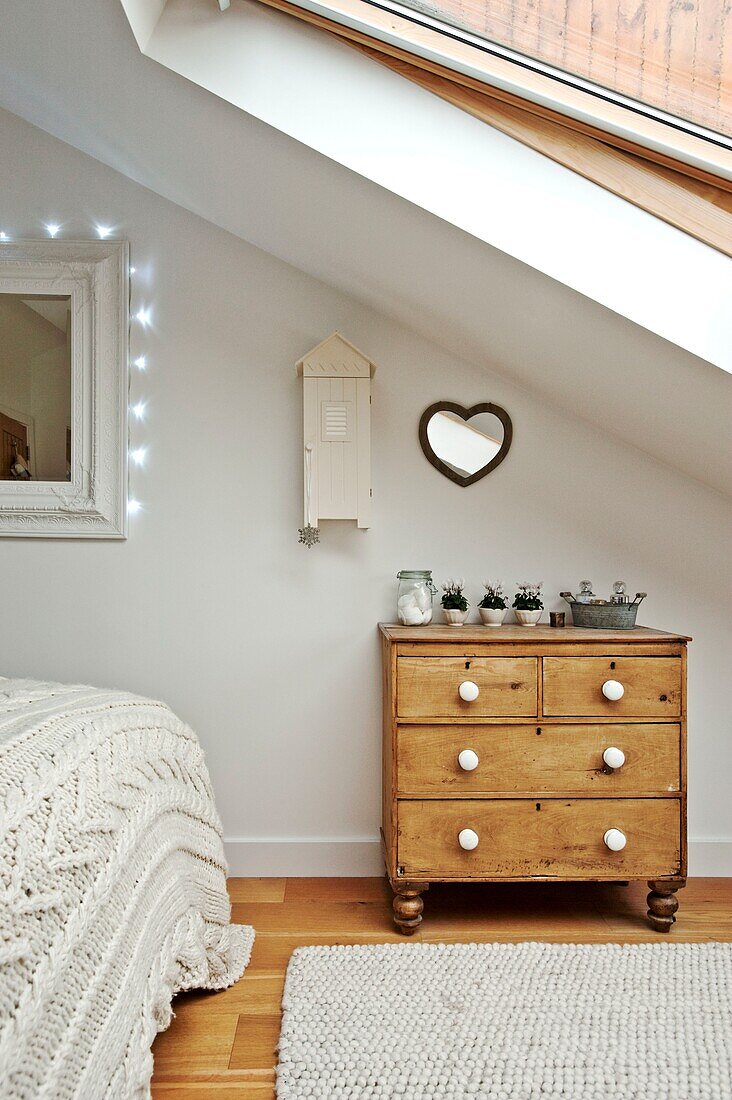 Heart shaped mirror above wooden chest of drawers in attic bedroom of Wadebridge family home, North Cornwall, UK