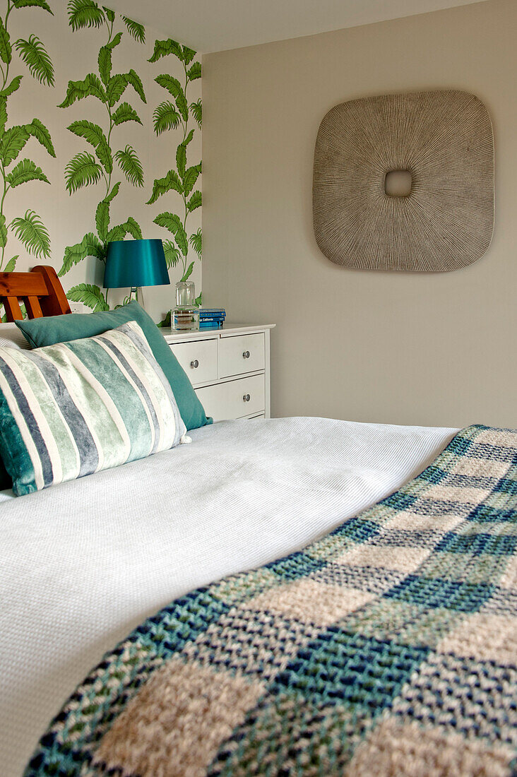 Karierte Decke auf einem Doppelbett in einem Zimmer mit blattgemusterter Tapete in einem Haus in Cornwall England