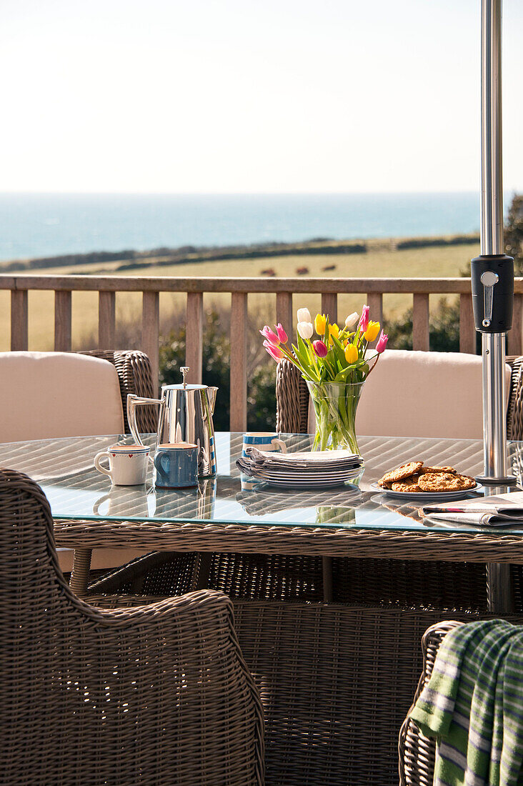 Kaffeekanne und Tulpen auf Glastisch mit Korbstühlen Cornwall UK