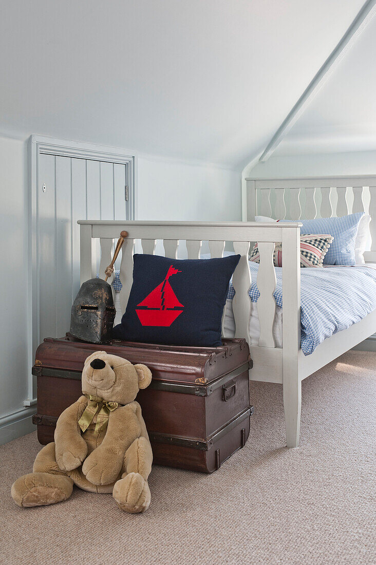 Teddy bear with vintage trunk at foot of single bed in attic room of family home, Cornwall, UK