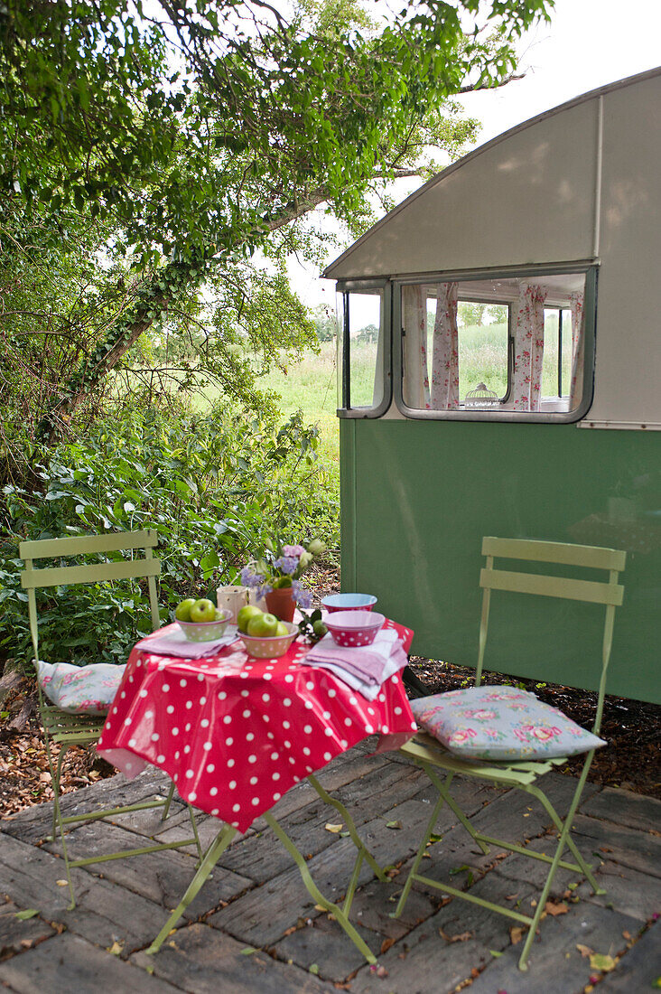 Folding chairs and table with red spotted tablecloth on caravan decking
