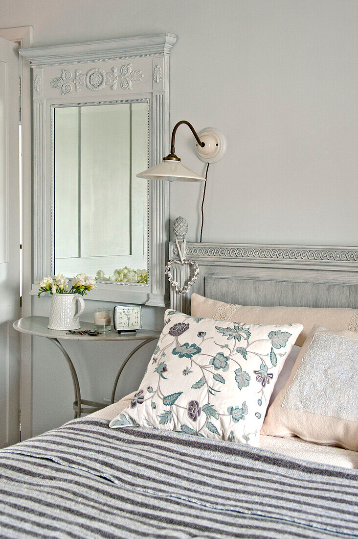 Kissen mit Blumendruck auf dem Bett mit Spiegel und Lampe in einem Haus in Crantock, Cornwall, England UK