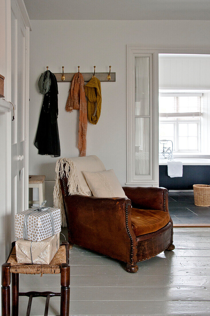 Brown leather armchair below coathooks in bedroom of Crantock home Cornwall England UK
