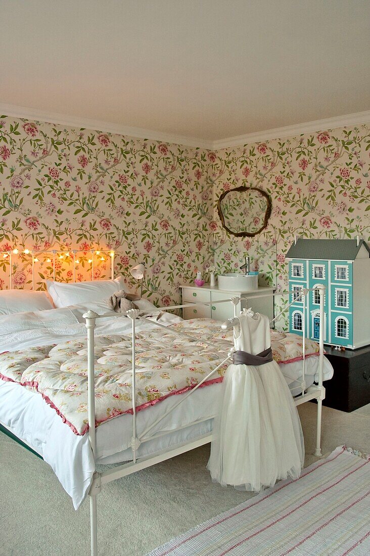 Weißes Kleid und Puppenhaus im Mädchenzimmer mit rosa Blumentapete in Penzance family home Cornwall England UK