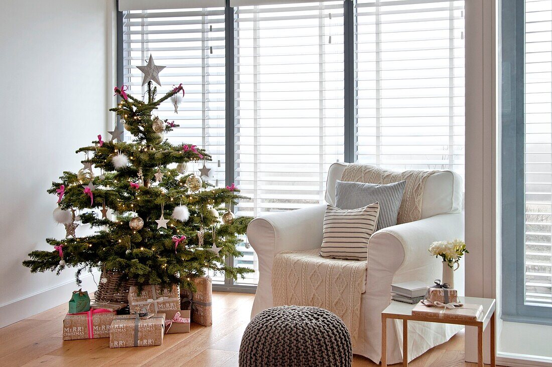 Eingepackte Geschenke unter dem Weihnachtsbaum mit weißem Sessel in einem Haus in Wadebridge, North Cornwall, UK