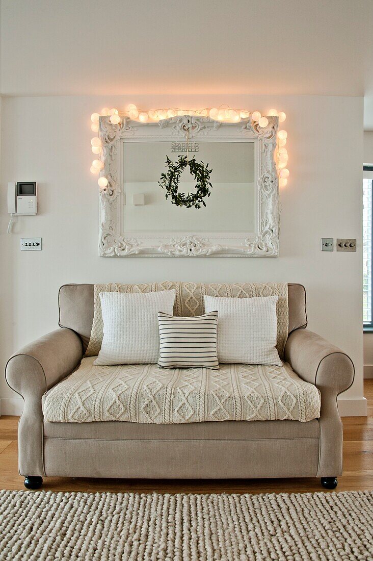 Lit lights on mirror above two seater sofa in Wadebridge home, North Cornwall, UK