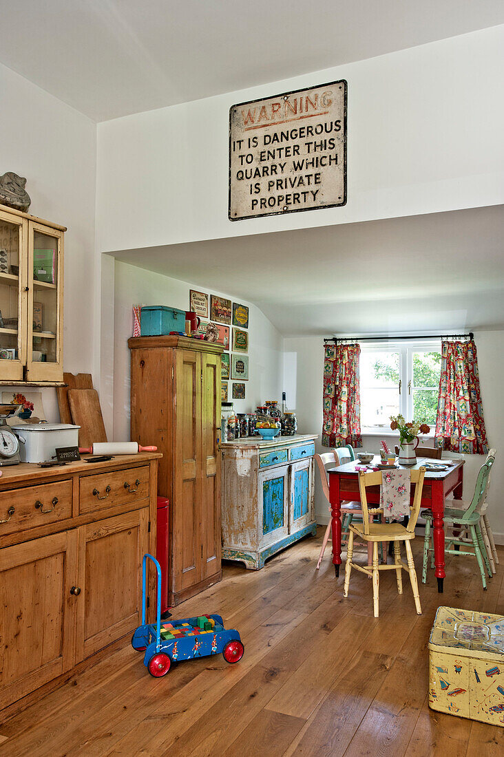 Wooden sideboard and salvaged quarry sign in open plan kitchen with painted table and chairs in Cambridge cottage England UK