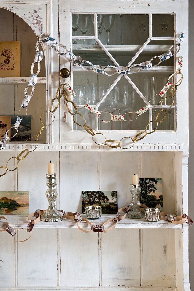 Papierketten mit silbernen Kerzenhaltern auf einer bemalten Kommode in einem Haus in London, England, UK