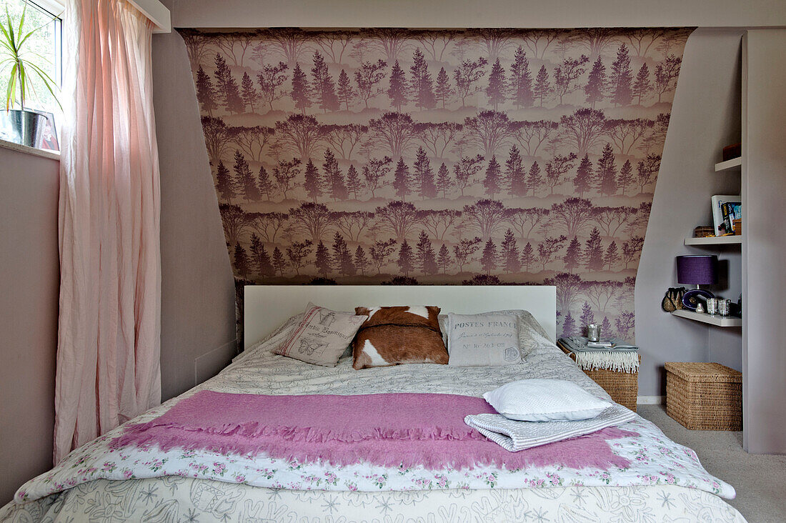Mustertapete über einem Doppelbett mit rosa Decke und Vorhängen in einem Einfamilienhaus in East Grinstead, West Sussex, England, UK