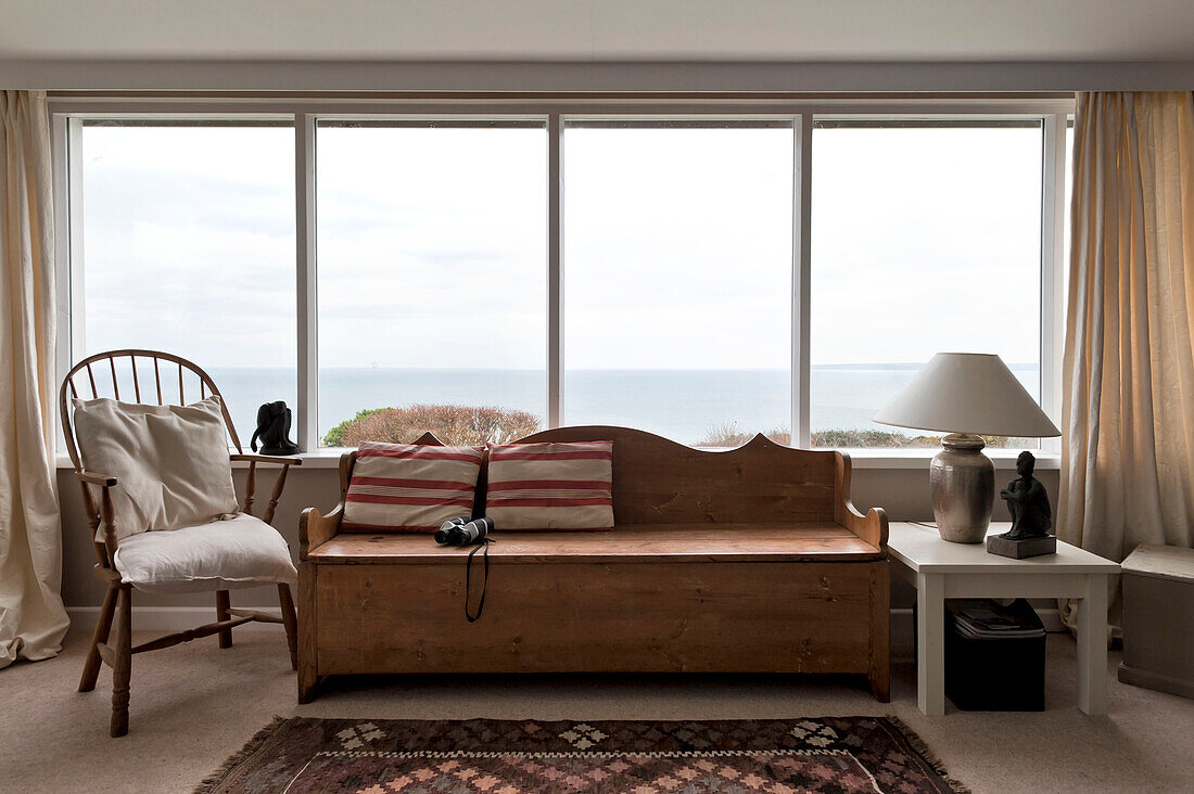 Striped cushion and binoculars on wooden bench seat in window of beach house Cornwall England UK