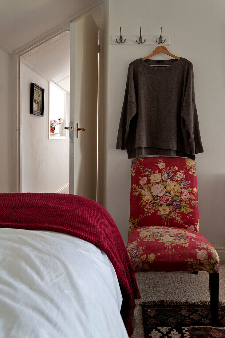 Brauner Pullover über rotem geblümten Stuhl im Einzelzimmer eines Strandhauses in Cornwall England UK