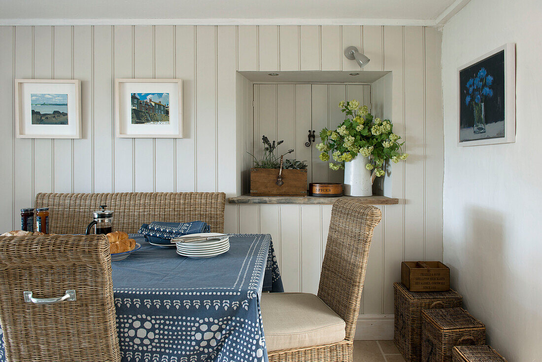 Frühstückstisch mit blauem Tischtuch und Korbstühlen in einer Bauernhausküche in Penzance, Cornwall, England, UK