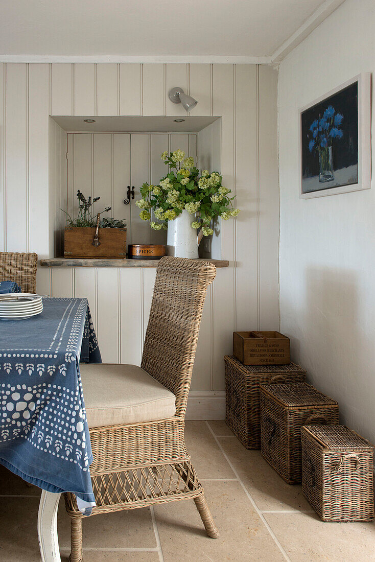 Korbstuhl und Körbe am Esstisch mit blauem Tischtuch in einem Bauernhaus in Penzance, Cornwall, England UK