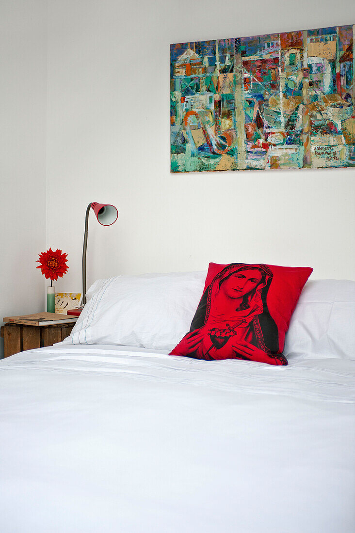 Artwork above double bed with side lamps and cushion with religious icon in townhouse bedroom Cornwall England UK