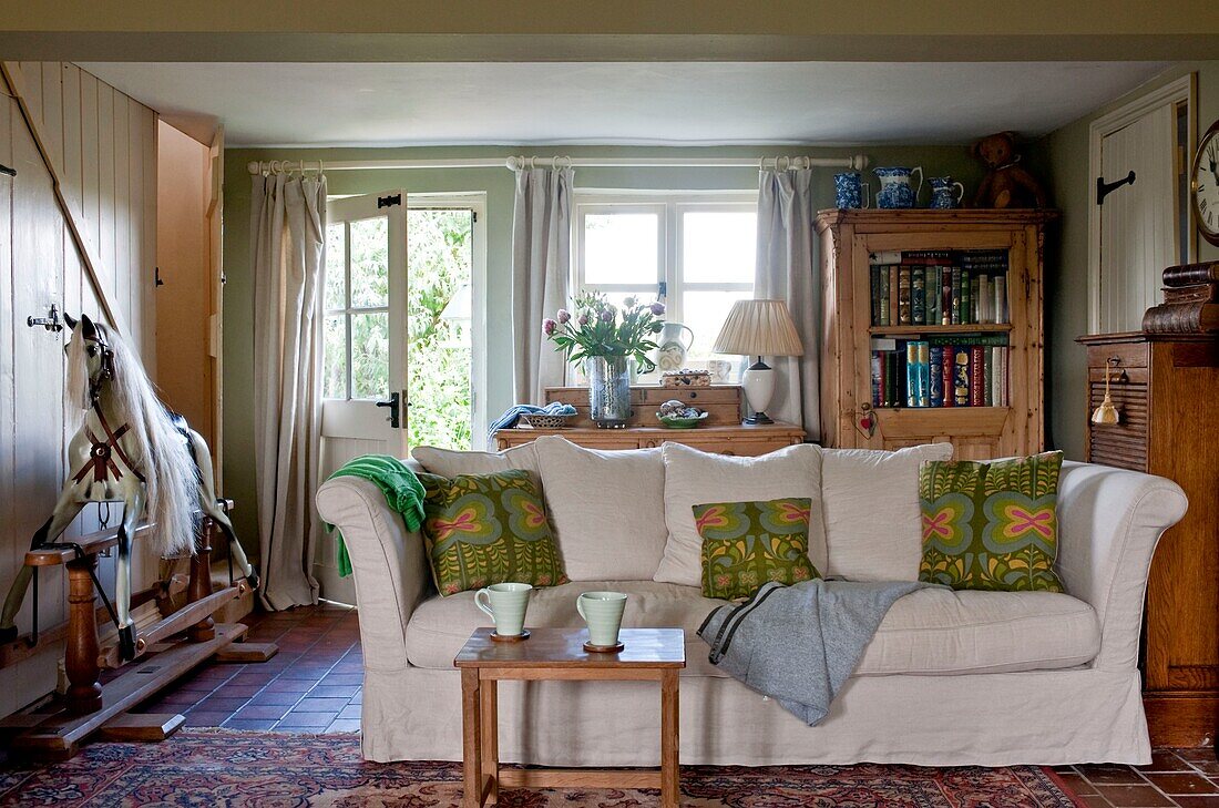 Tassen auf dem Tisch vor dem Sofa mit Schaukelpferd im Wohnzimmer von Edworth, Bedfordshire, England UK