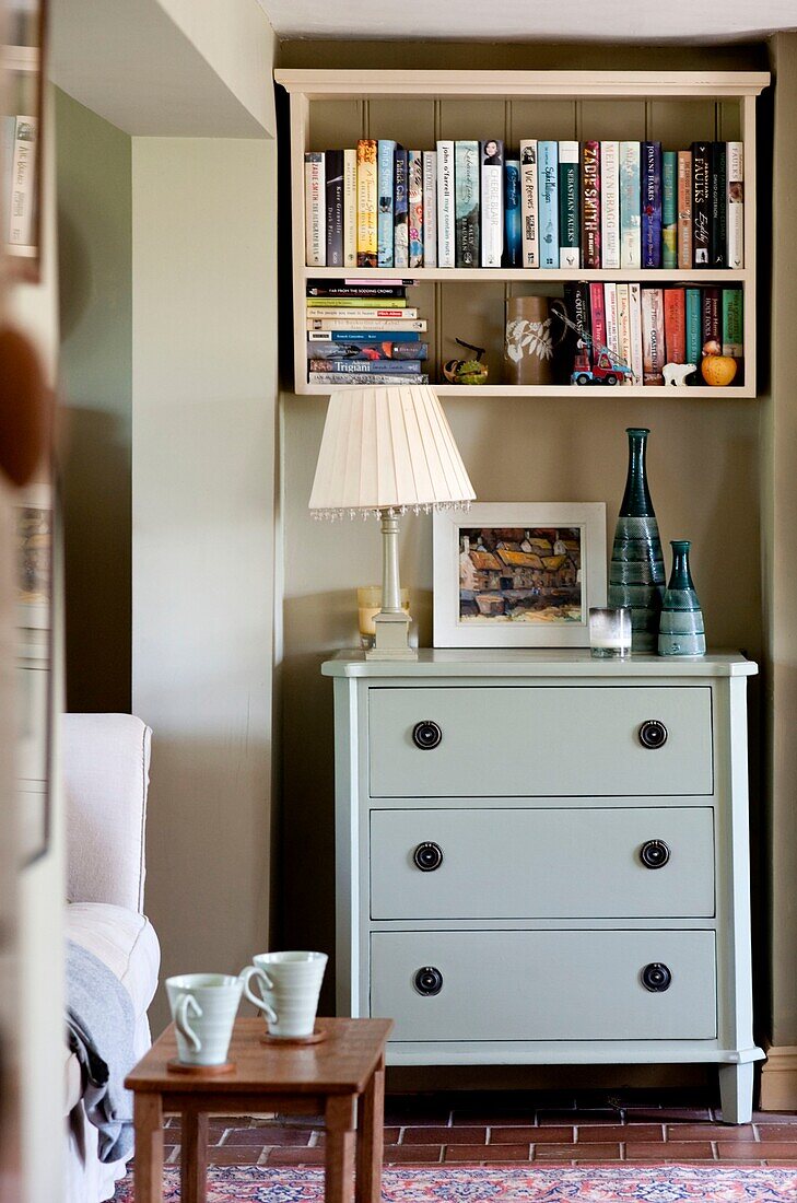 Wall-mounted bookshelf above pale green chest of drawers in Edworth living room Bedfordshire England UK