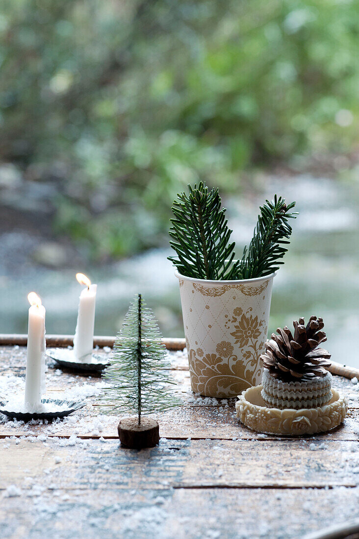 Ein Weihnachtsbaum als Kuchendekoration mit gemusterten Pappbechern, Tortenböden, Zapfen, Kerzenlicht und künstlichem Schnee