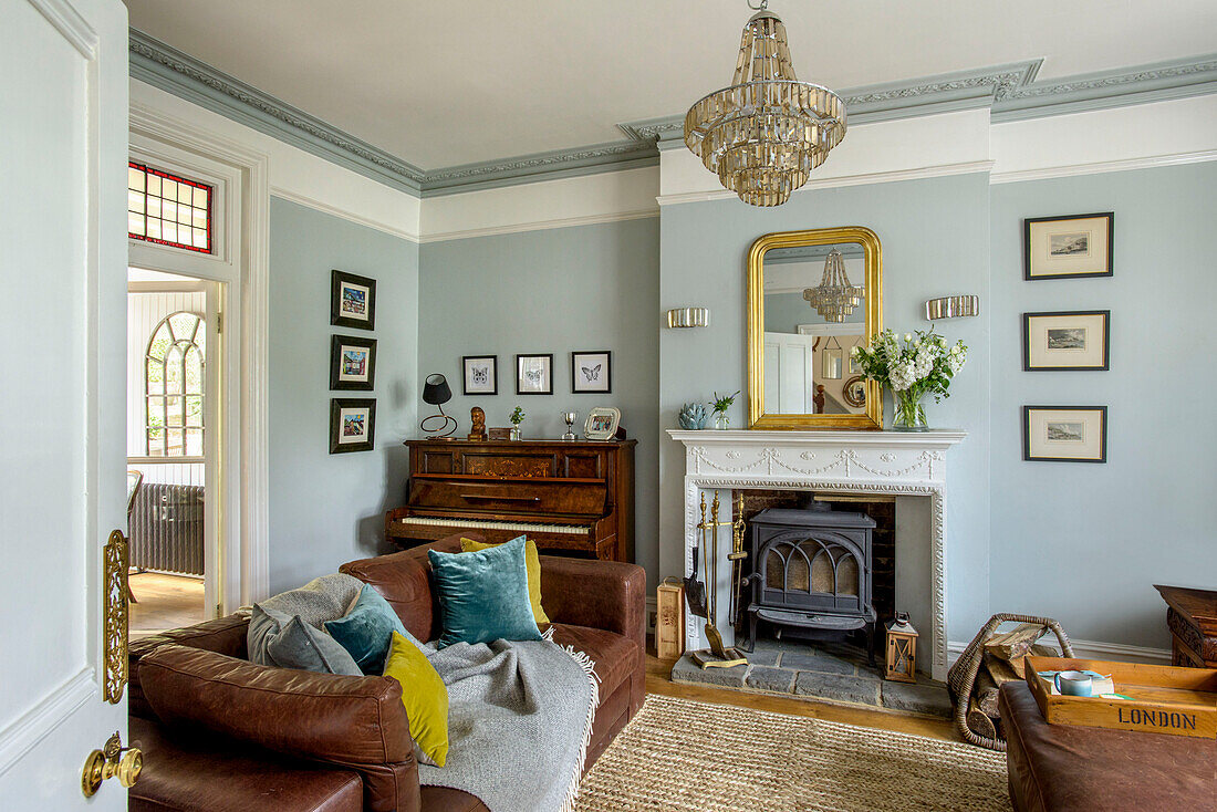Braunes Ledersofa in hellblauem Wohnzimmer mit Glaslüster und Klavier in einem Einfamilienhaus in Tunbridge Wells, Kent, England, UK