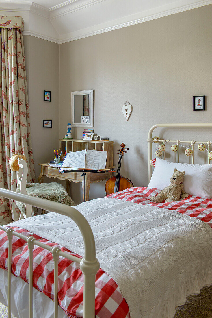 Rot-weiß karierte Bettdecke auf metallgerahmtem Einzelbett mit Cello im Mädchenzimmer eines Hauses in Tunbridge Wells, Kent, England, UK
