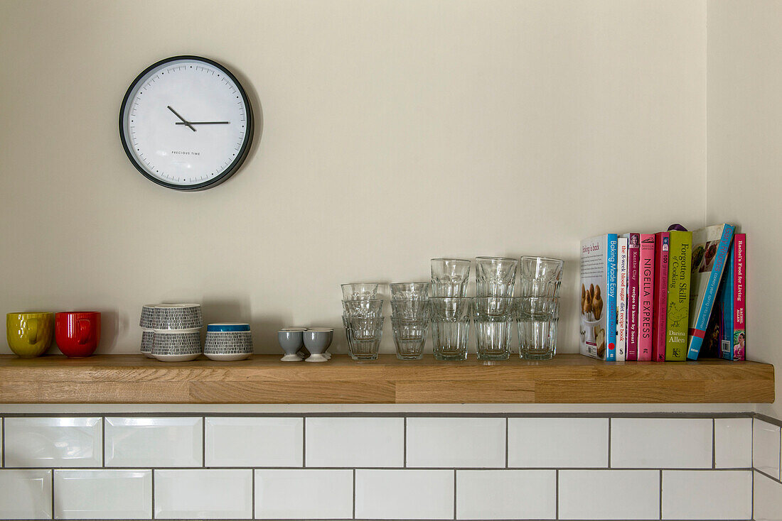 Rezeptbücher und Glaswaren mit Uhr und Schalen auf einem Küchenregal in St Ives, Cornwall, Vereinigtes Königreich