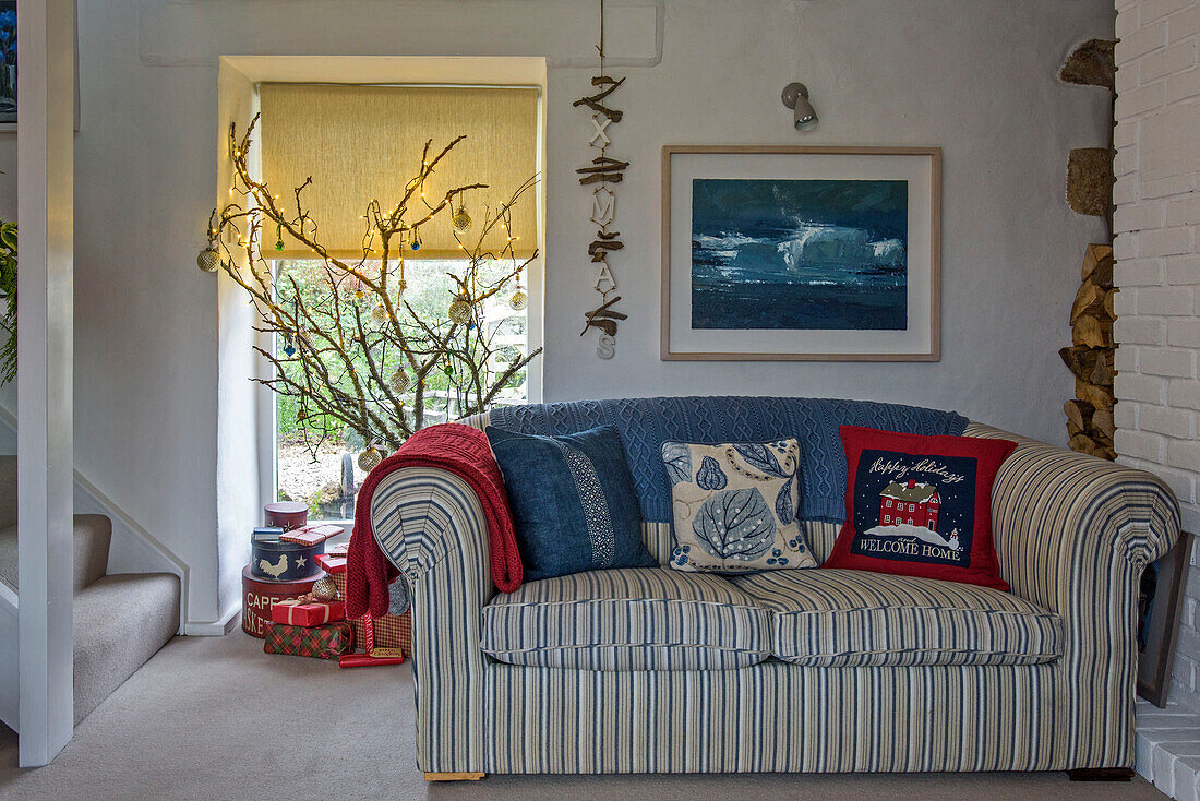 Gestreiftes Sofa mit blauer Decke unter gerahmtem Kunstwerk mit Weihnachtsdekoration in einem Bauernhaus in Penzance, Cornwall, Großbritannien