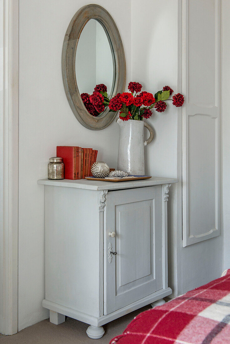 Rote Schnittblumen und runder Spiegel auf Anrichte in Schlafzimmer in Penzance, Cornwall, UK