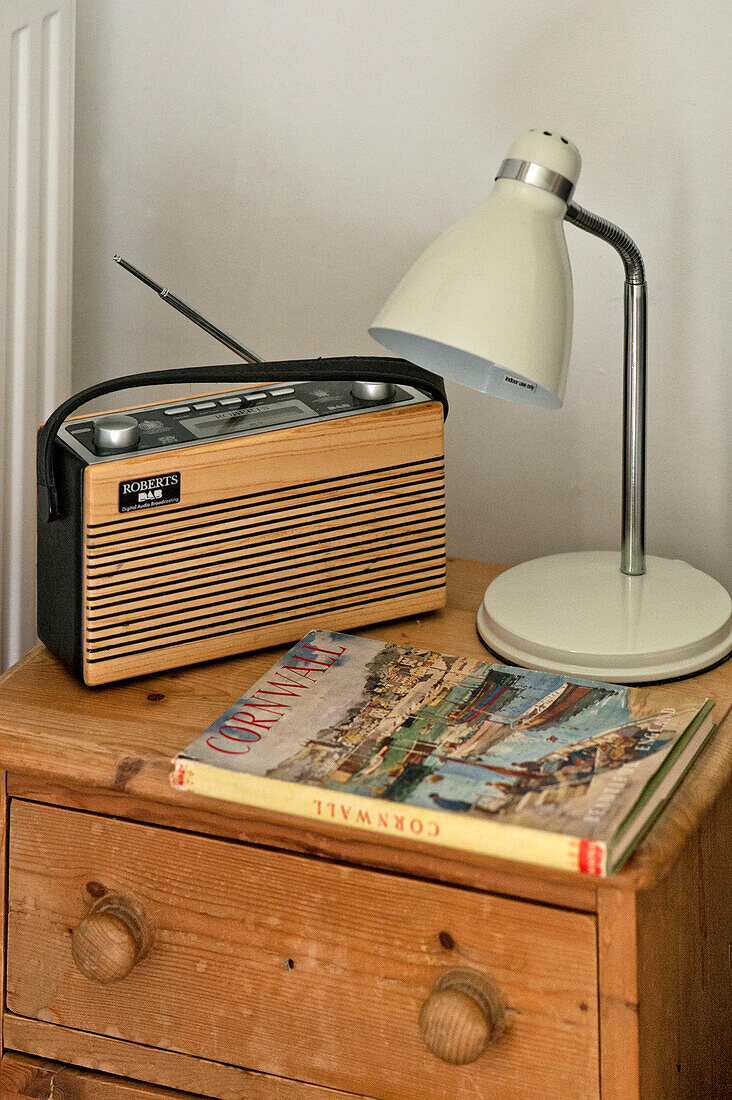 Radio book and bedside lamp on wooden chest of drawers in Cornwall cottage Cornwall UK