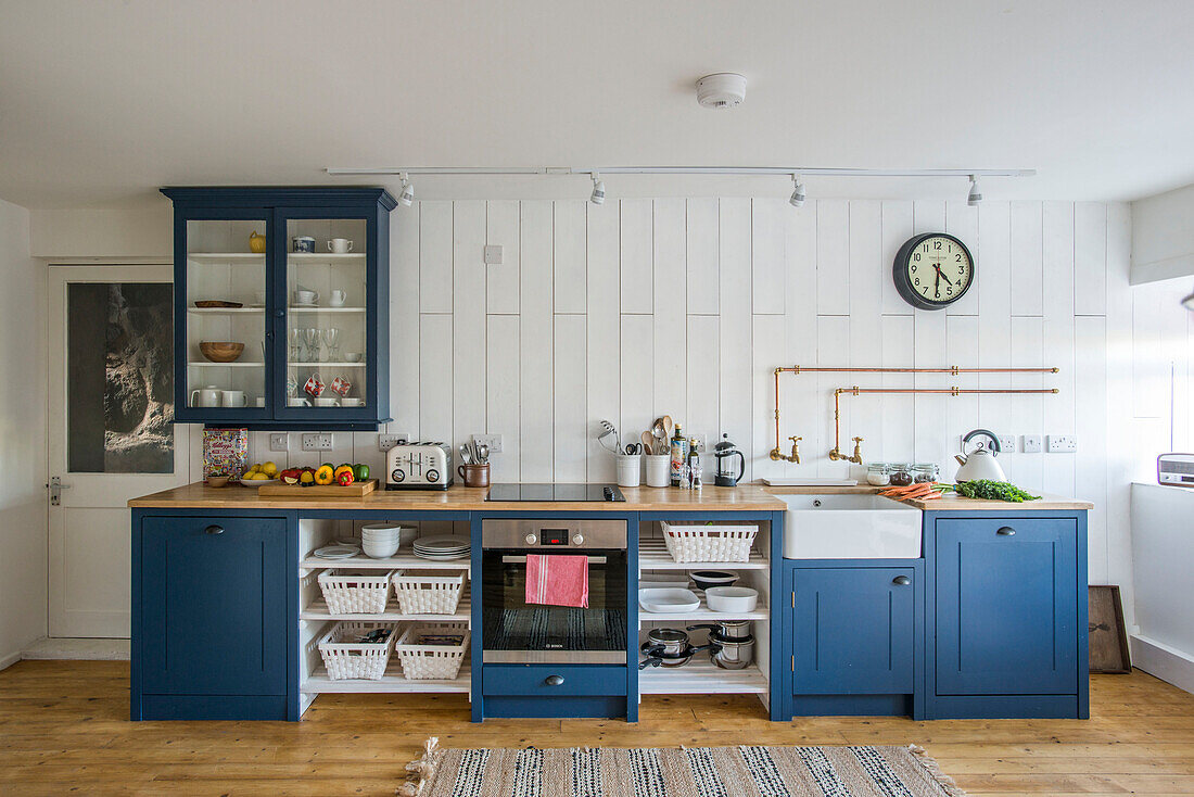 Blue fitted kitchen with homeware in panelled Cornwall cottage UK