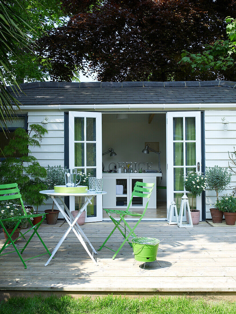 Tisch mit grünen Klappstühlen auf der Terrasse eines Sommerhauses und Arbeitsateliers in Großbritannien