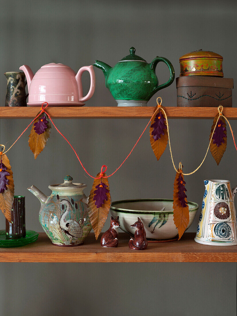 Assorted teapots with leaf decoration on wooden shelf in UK home
