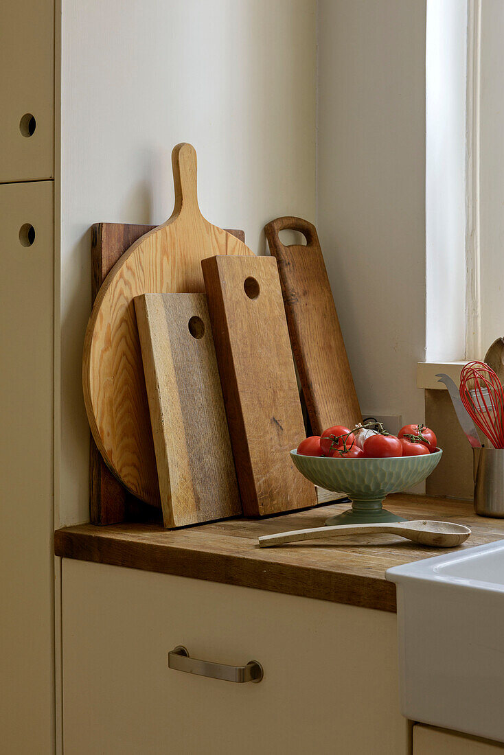 Bowl of tomatoes and wooden spoon with chopping boards on worktop in London kitchen UK