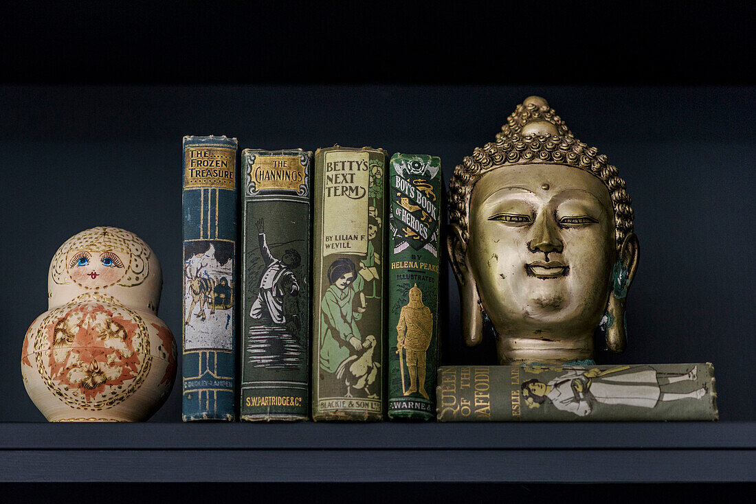Vintage-Bücher und Buddhakopf auf schwarzem Regal im Haus in Godalming Surrey UK
