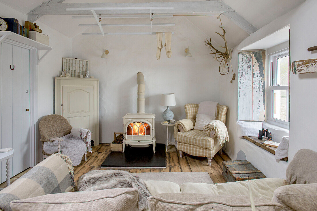 Checked sofa beside lit woodburning stove in living room of Marazion beach house Cornwall UK