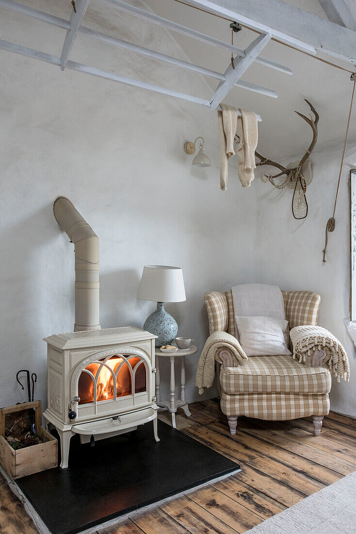 Checked armchair with lit woodburning stove in living room of Marazion beach house Cornwall UK