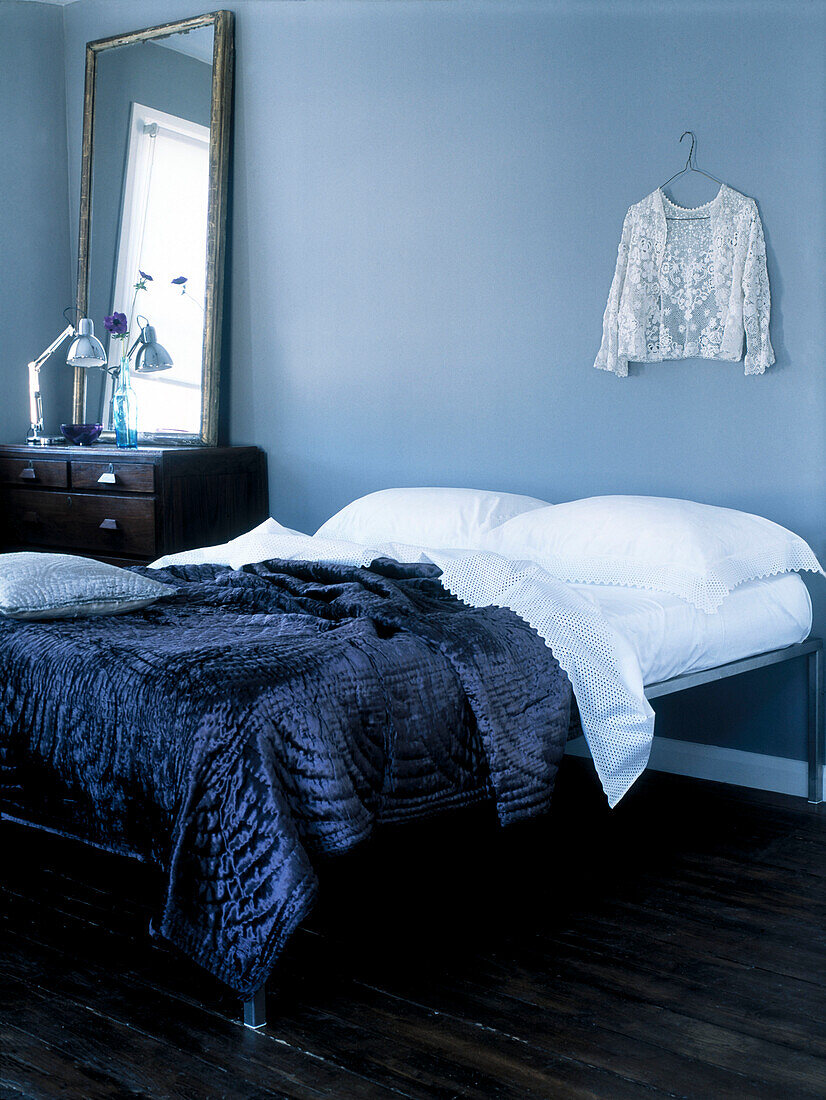 Ungepolstertes Doppelbett mit Satinbettdecke und Spitzenmieder und dunklen Holzdielen in einem hellblauen Schlafzimmer