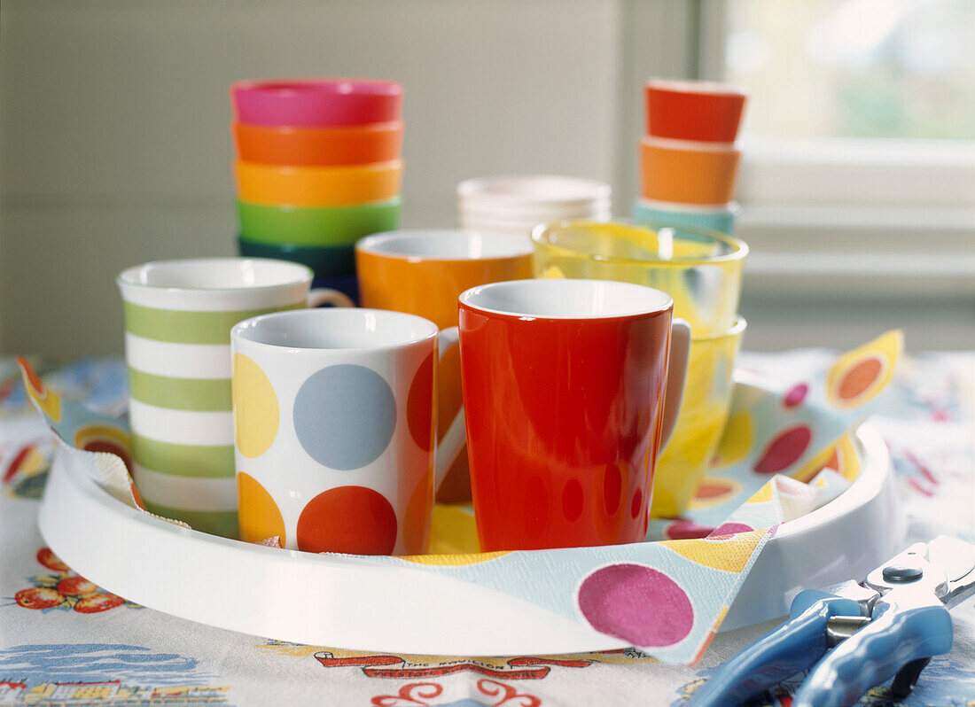 Colourful display of mismatched mugs and beakers on a plastic tray 